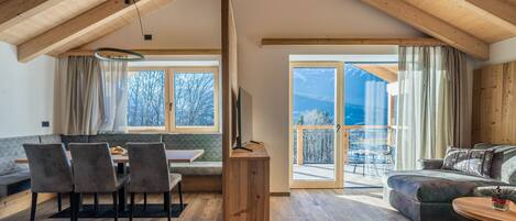 Un loft spacieux avec de hauts plafonds, des poutres apparentes, un coin repas avec une banquette, un canapé et un balcon offrant une vue dégagée.