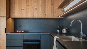 A modern kitchen with wooden cabinets, a black countertop, a built-in oven, a sink, and a kettle.