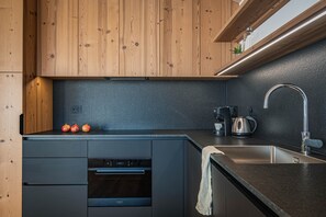 Une cuisine moderne avec des meubles en bois, un plan de travail noir, un four encastré, un évier et une bouilloire.