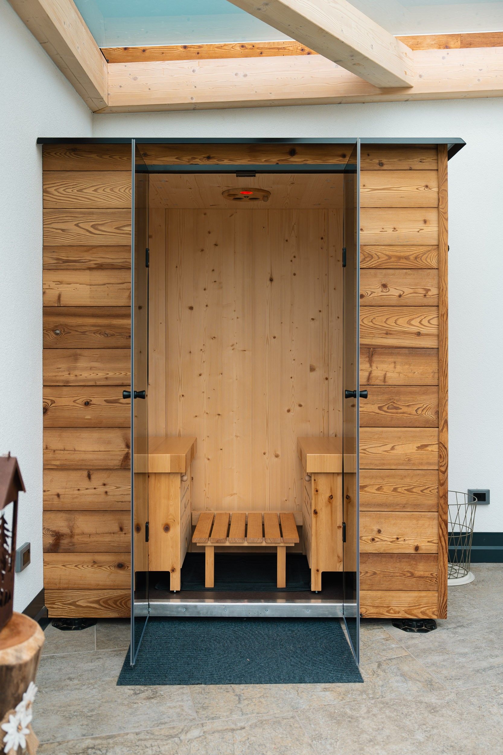 A wooden sauna with benches and a bench seat, a metal door, and a skylight above.