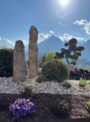 Un jardín con formaciones rocosas, un pino y montañas al fondo.