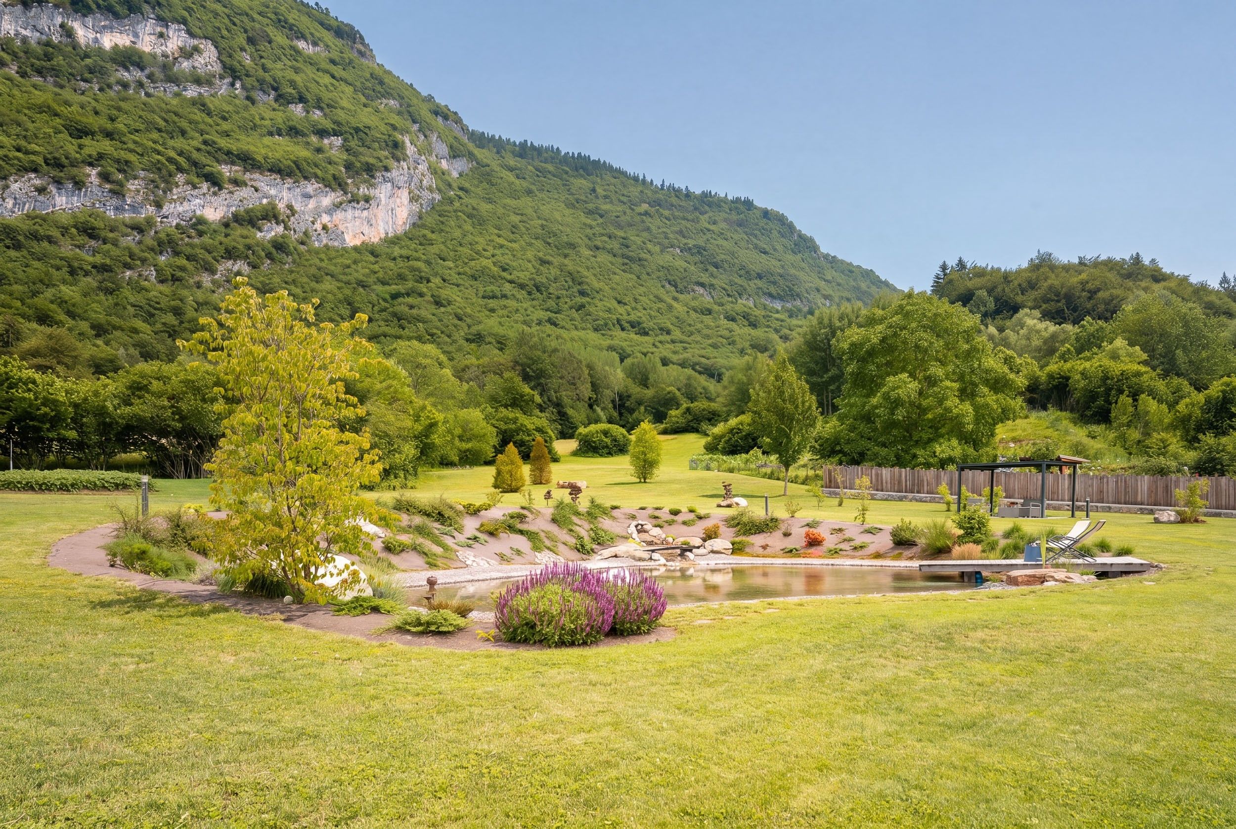 Un jardín ajardinado con un estanque, zona de estar y vistas a un paisaje montañoso.