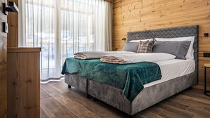 A bedroom with a bed, wooden walls, a window with curtains, and a wooden floor.