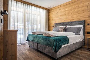 A bedroom with a bed, wooden walls, a window with curtains, and a wooden floor. - Apartment 'Larice' with Mountain View, Wi-Fi and Air Conditioning (Cavedago)