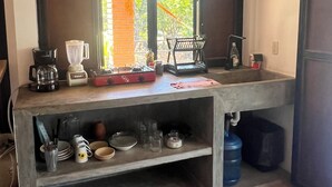 Una cocina con ventana, cafetera, licuadora, hervidor y lavamanos.