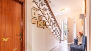 Una puerta de madera con adhesivos de mariposas, una escalera con barandillas metálicas decorativas y un sillón azul con cojín.