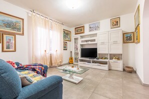 A living room with a sofa, a glass coffee table, a TV, and white cabinets. - Holiday Home 'Giuliana' with Private Terrace, Private Garden and Wi-Fi (Poggio a Caiano)