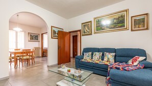 Una sala de estar con una mesa de centro de vidrio, un sofá azul y cuadros en la pared.