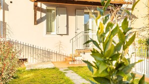 Una casa con techo de tejas, contraventanas blancas, una escalera de madera y un patio cercado.
