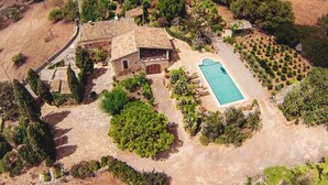 Vista aérea de una propiedad con piscina, edificios de piedra y vegetación circundante.