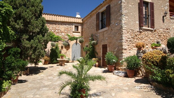 Edificio de piedra con patio, plantas en macetas y puerta de madera.