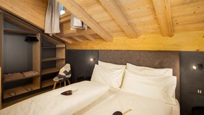 Eine Holzbalkendecke, ein Bett mit weißer Bettwäsche, ein Stuhl, ein Schuhregal und eine Wandleuchte.