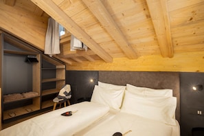 Eine Holzbalkendecke, ein Bett mit weißer Bettwäsche, ein Stuhl, ein Schuhregal und eine Wandleuchte.