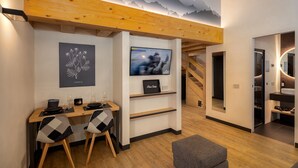 Ein modernes Wohnzimmer mit Holzboden, einem Flachbildfernseher, einer Essecke mit zwei Stühlen und einer Treppe, die in einen anderen Raum führt.