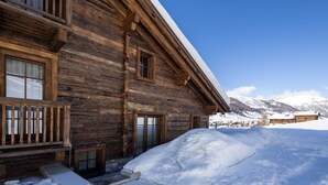 Eine Holzhütte mit verschneitem Gelände und Bergen im Hintergrund.