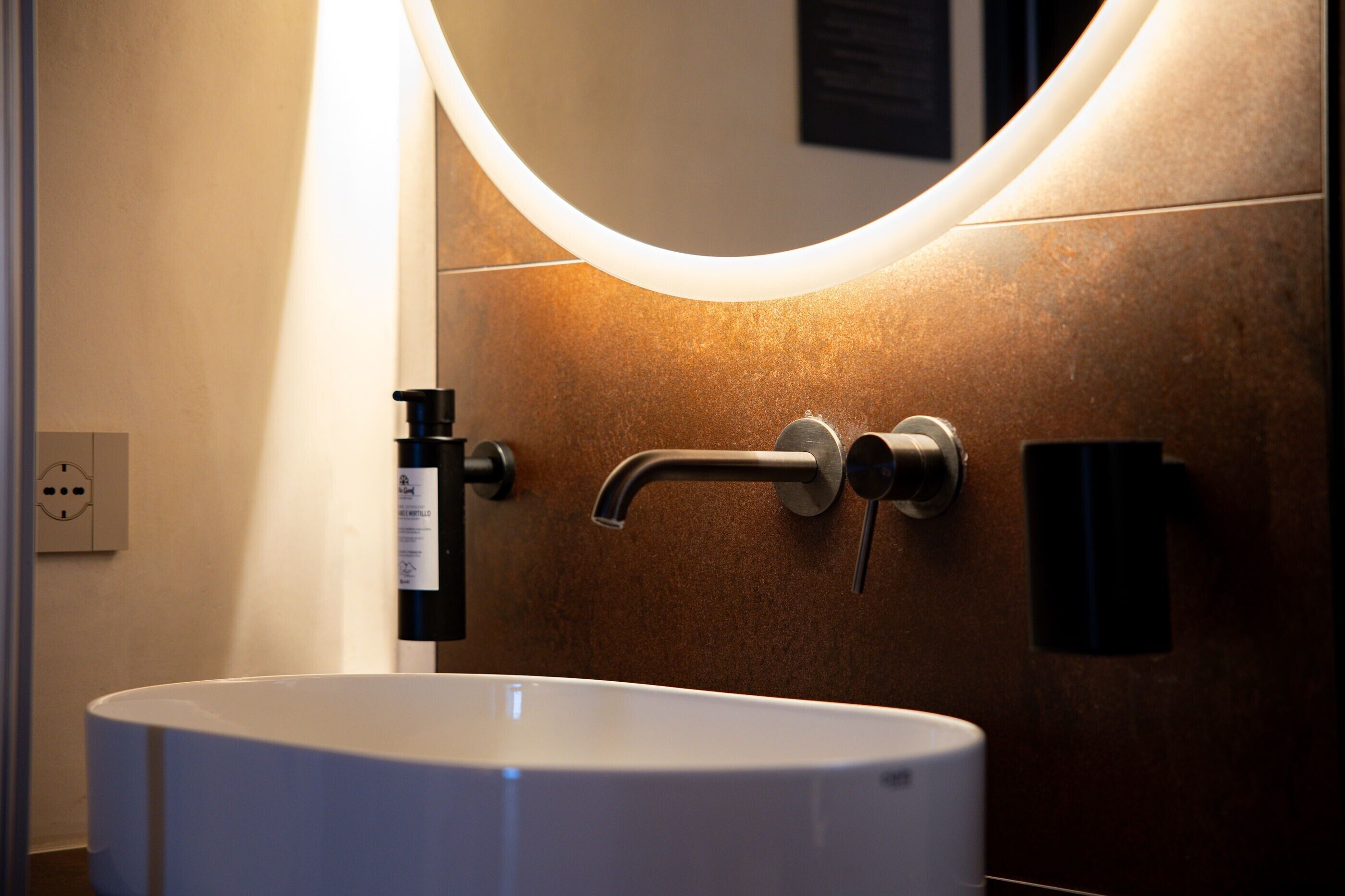 Une salle de bain avec un lavabo blanc, un miroir incurvé et un robinet fixé au mur.