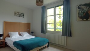 A bedroom with a bed, a nightstand, a window with curtains, and a wall-mounted artwork. - Château des Gipières, exceptional apartment: Private Garden, Pool, View of Mont Ventoux (Montbrun-les-Bains)