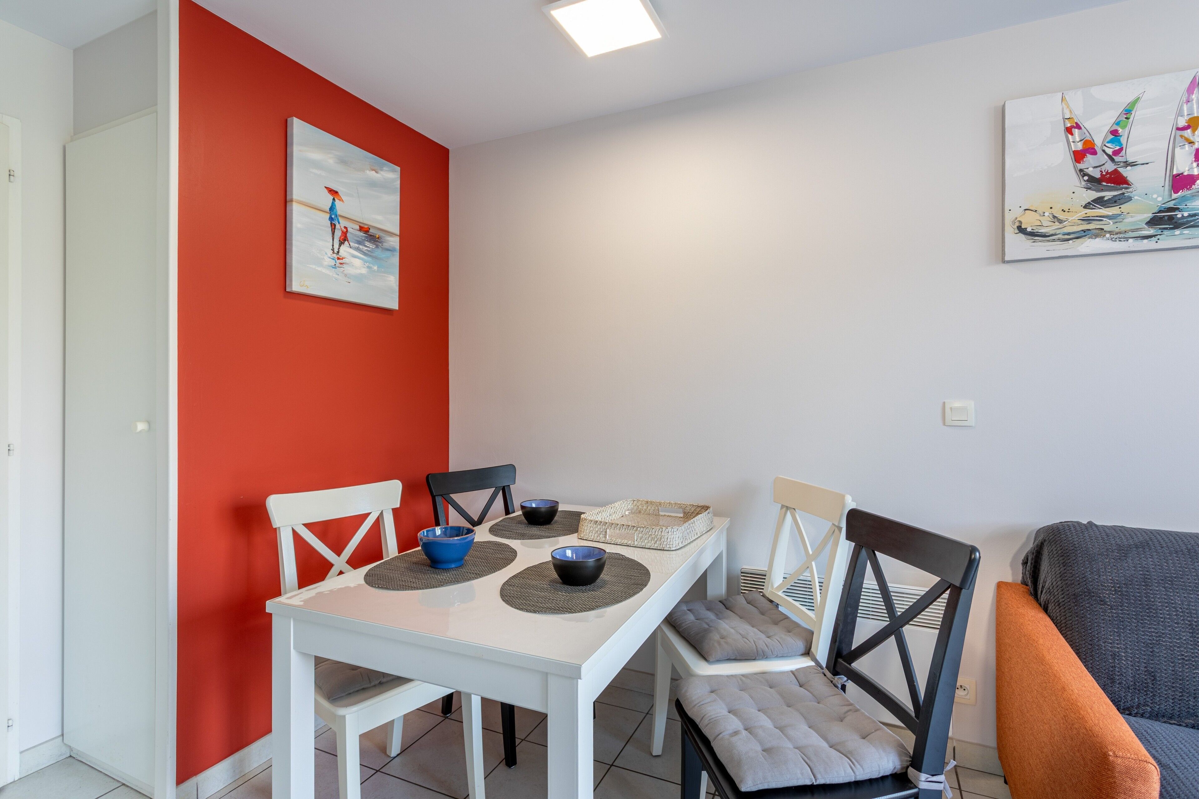 Een eetruimte met een witte tafel, zwarte stoelen en een rode accentmuur.