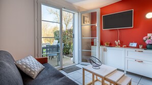 Una sala de estar moderna con sofá, una mesa de comedor y una zona de cocina con televisor y armarios.