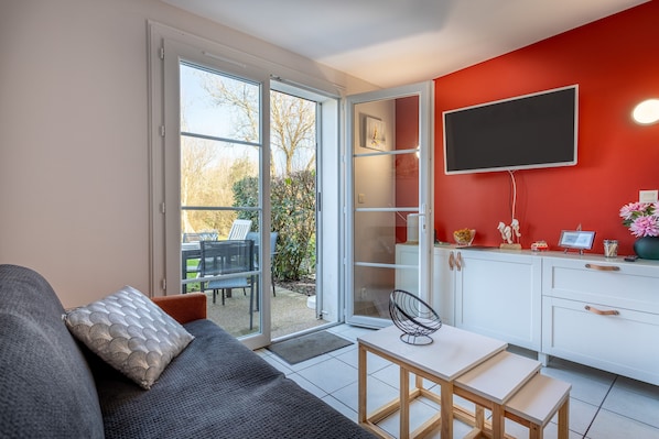 A modern living room with a sofa, a dining table, and a kitchen area with a TV and cabinets.