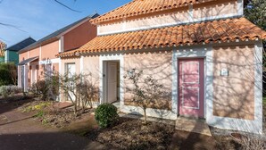 Un edificio de dos pisos con techo de tejas, un pequeño jardín y una puerta con placa de número.