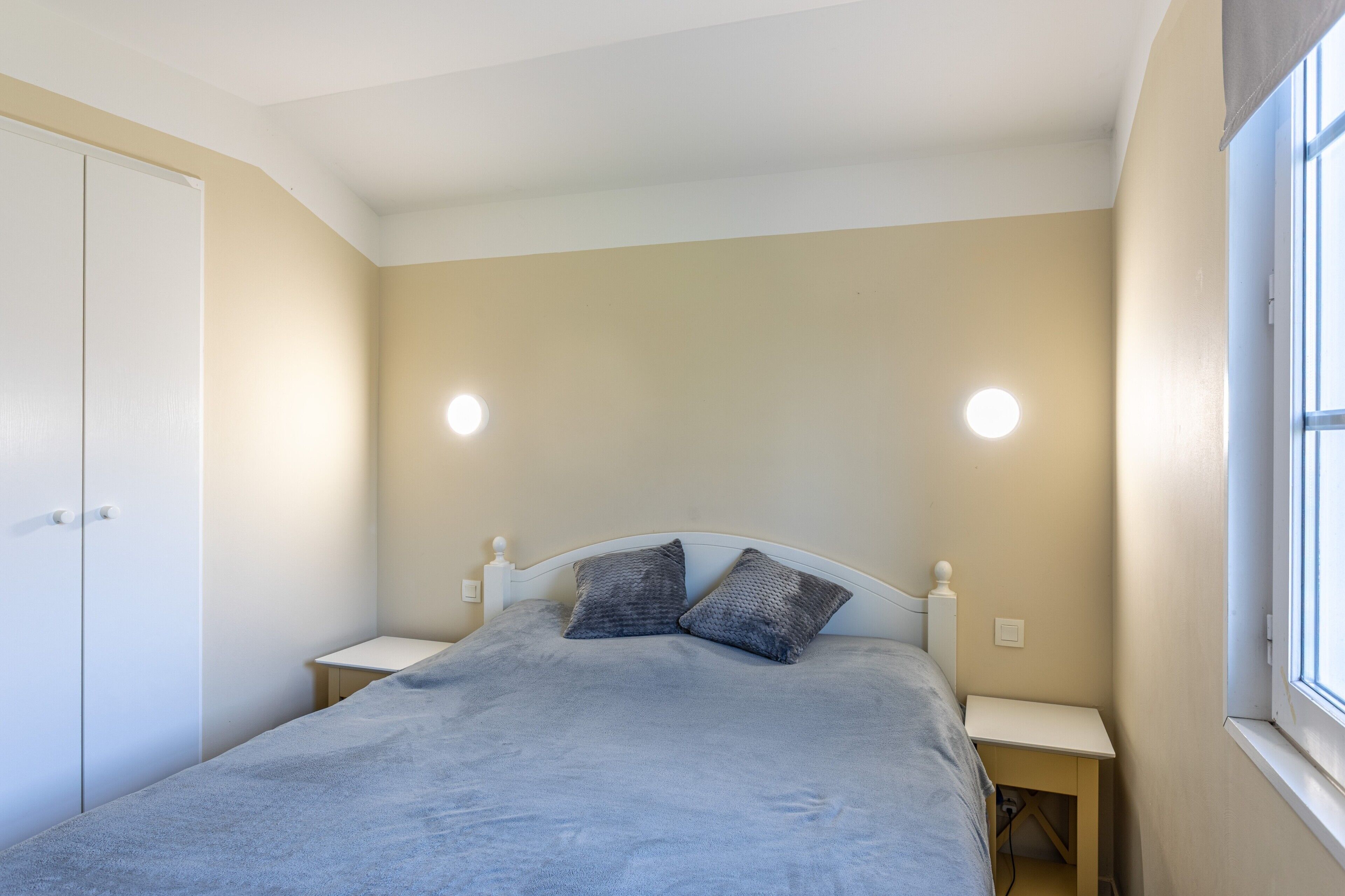 A bedroom with a bed, two bedside tables, a wardrobe, and a window.