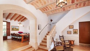 A spacious dining area with a wooden table and chairs, a staircase with a white railing, and a rustic ceiling. - Country House 'Magdalena - Son Gaya' with Private Pool, Wi-Fi and Air Conditioning (Illes Balears)