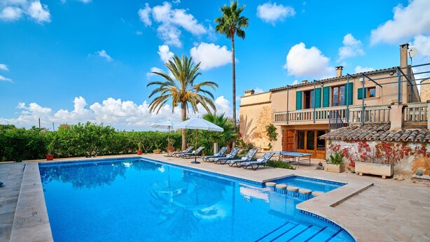 A swimming pool with lounge chairs, a palm tree, and a building with a balcony. - Country House 'Magdalena - Son Gaya' with Private Pool, Wi-Fi and Air Conditioning (Illes Balears)