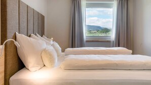 A hotel room with a bed, pillows, a headboard, a window with curtains, and a view of a landscape. - Apartment 'Hans' with Mountain View, Private Garden and Wi-Fi (Cornedo all'Isarco)