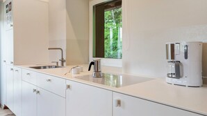 A modern kitchen with white cabinetry, a stainless steel sink, a coffee maker, and a window with a view of trees. - Apartment 'Hans' with Mountain View, Private Garden and Wi-Fi (Cornedo all'Isarco)