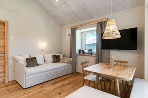 A modern living room with a sofa, dining table, chairs, a TV, and a view of the outdoors. - Apartment 'Hans' with Mountain View, Private Garden and Wi-Fi (Cornedo all'Isarco)