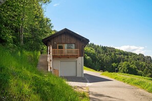 A wooden cabin with a balcony, a garage, and a forested hillside. - Apartment 'Hans' with Mountain View, Private Garden and Wi-Fi (Cornedo all'Isarco)