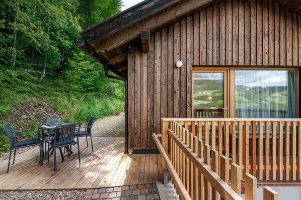 Una caba ña de madera con terraza, mobiliario exterior y vistas al bosque circundante.