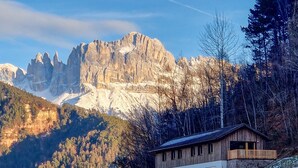A mountain cabin with a wooden exterior, a stone foundation, and a balcony overlooking a snowy landscape with a mountain backdrop. - Apartment 'Hans' with Mountain View, Private Garden and Wi-Fi (Cornedo all'Isarco)