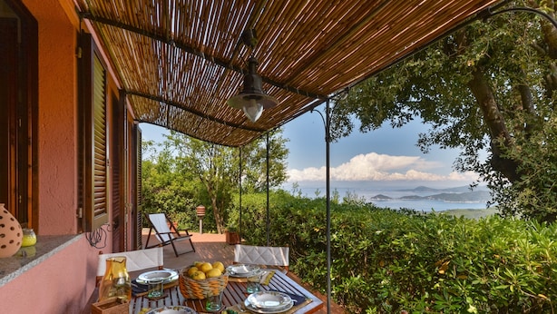An outdoor dining area with a table set for two, a wicker basket with lemons, and a view of the sea. - Villa 'Martini' with Sea View, Private Terrace and Wi-Fi (Marciana)