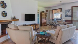 A living room with a sofa, a television, a fireplace, and a dining area with a table and chairs. - Villa 'Martini' with Sea View, Private Terrace and Wi-Fi (Marciana)