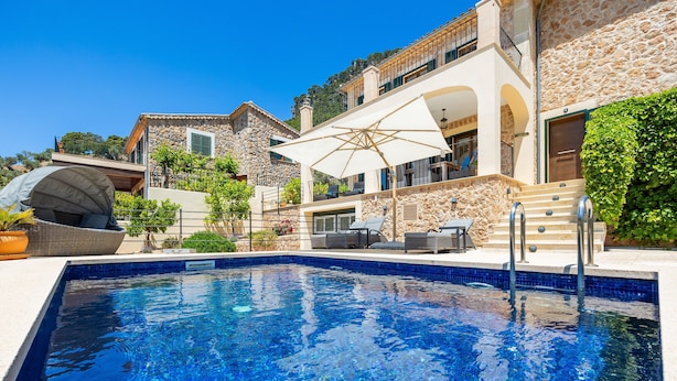 A swimming pool with a stone facade, outdoor furniture, and a large umbrella. - Villa 'Sa Papaiona' with Mountain Views, Private Pool and Wi-Fi (Valldemossa)