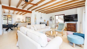 A spacious living area with a sofa, ottomans, a coffee table, and a TV. - Villa 'Sa Papaiona' with Mountain Views, Private Pool and Wi-Fi (Valldemossa)