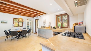 A modern kitchen with a central island, a dining area with chairs, and a large window providing natural light. - Villa 'Sa Papaiona' with Mountain Views, Private Pool and Wi-Fi (Valldemossa)
