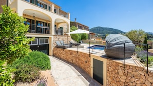 A villa with a stone wall, outdoor seating, a pool, and a view of hills. - Villa 'Sa Papaiona' with Mountain Views, Private Pool and Wi-Fi (Valldemossa)