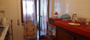 Une cuisine équipée d’une cuisinière à gaz, d’une bouilloire, d’un four à micro-ondes, d’une table rouge recouverte d’une plaque de verre et d’une assiette contenant de la nourriture.