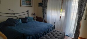Une chambre à coucher avec un lit, une table de chevet, une lampe, des rideaux et un tableau au mur.