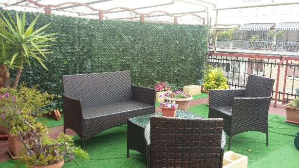 Un espace patio aménagé avec des meubles en osier, une pelouse artificielle verte et un mur végétal.