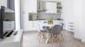 Une cuisine moderne avec des meubles blancs, une table à manger avec des chaises, un téléviseur et une petite plante posée sur le comptoir.