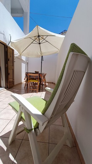 A patio with a white chair, a table, and a large umbrella. - Apartment 'Mi Casa Es Tu Casa - Piano Terra' with Private Terrace, Wi-Fi and Air Conditioning (Donnalucata)
