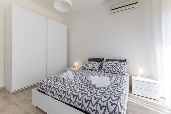A bedroom with a bed, nightstands, a wardrobe, and an air conditioning unit. - Apartment 'Mi Casa Es Tu Casa - Piano Terra' with Private Terrace, Wi-Fi and Air Conditioning (Donnalucata)