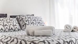 Un lit avec une literie à motifs, des serviettes enroulées et des oreillers décorés de motifs en forme de cœur.