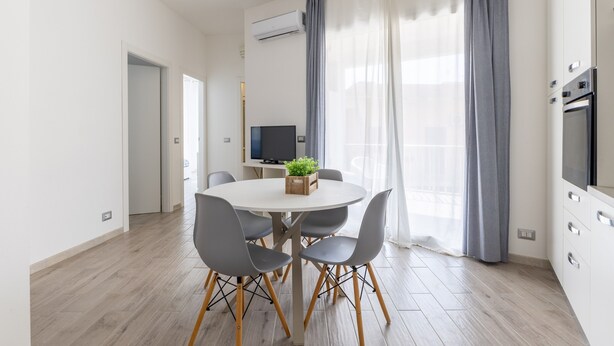 Une cuisine moderne dotée d’un four encastré, un coin repas avec une table ronde et des chaises, et une grande fenêtre avec des rideaux.