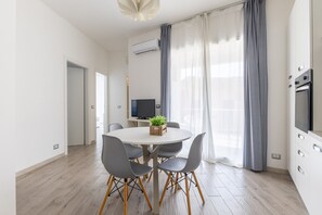 Une cuisine moderne dotée d’un four encastré, un coin repas avec une table ronde et des chaises, et une grande fenêtre avec des rideaux.