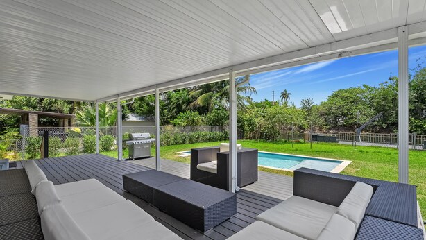 Eine Außenpatio mit überdachter Sitzgruppe, einem Pool und üppiger Bepflanzung im Hintergrund.